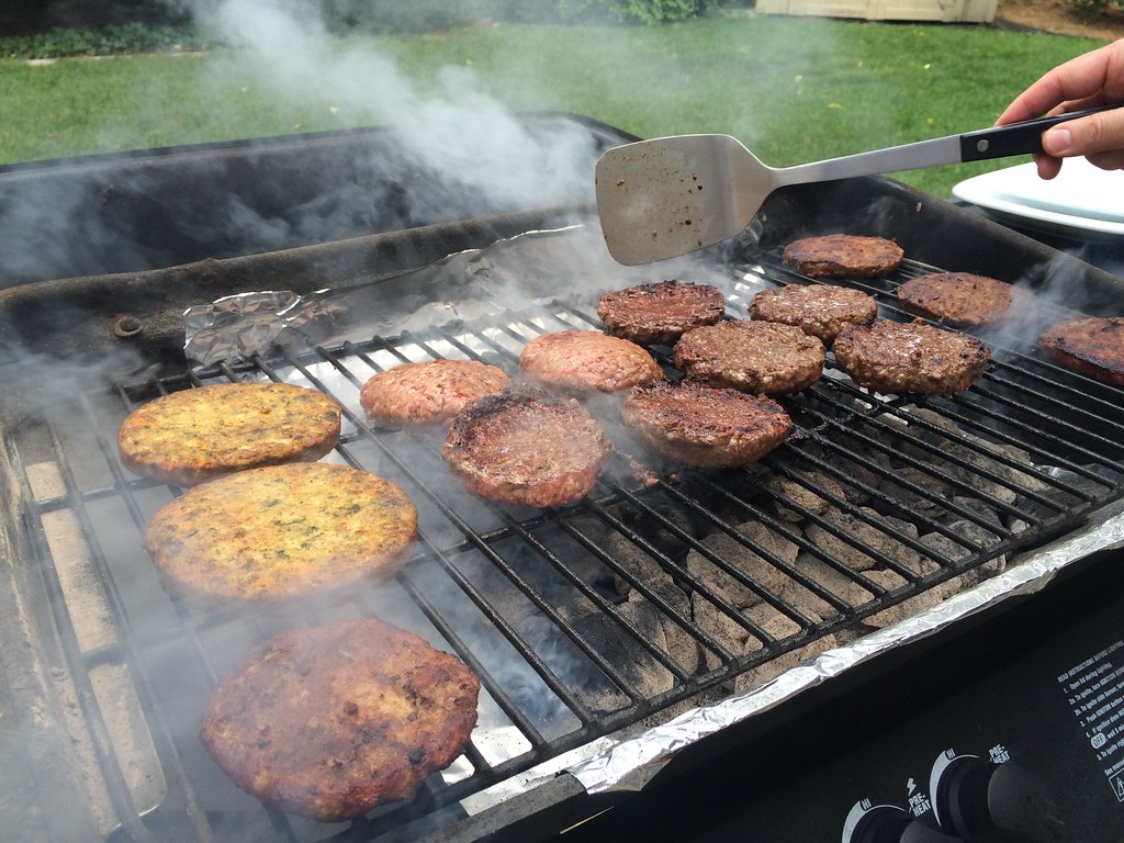 veggie burgers and beef burgers grilling on a barbecue.