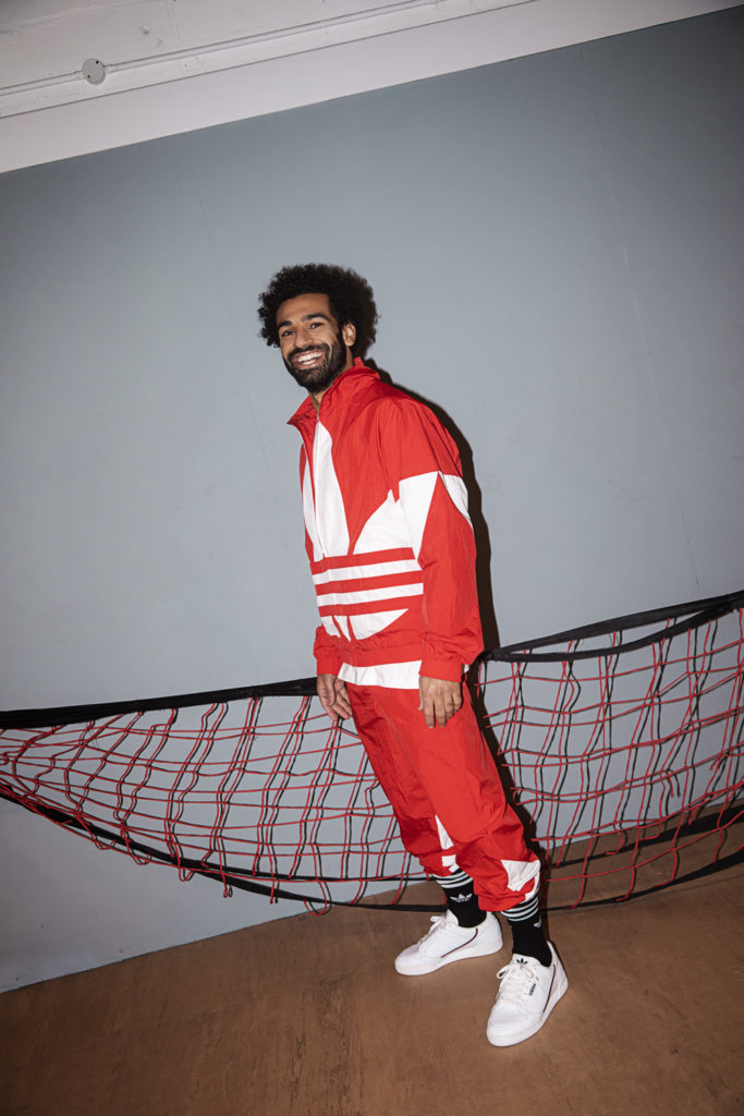 Mo Salah striding while wearing an Adicolor tracksuit in red and white.