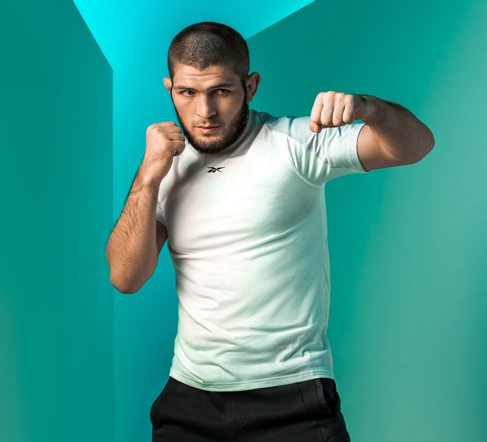 Khabib Nurmagomedov wearing white Reebok training top and black training trousers performing a left hook.
