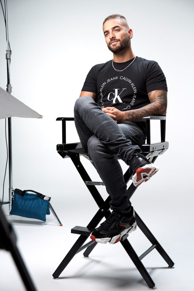 Maluma in Calvin Klein clothing sat in a directors chair.