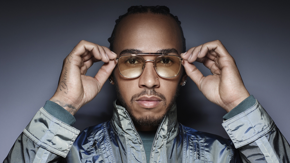 Lewis Hamilton holding a pair of Police sunglasses to his eyes.